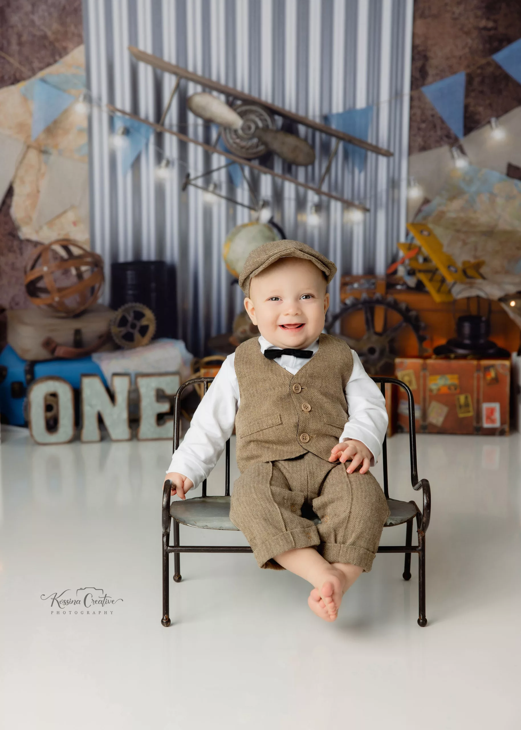 Orlando Boy Cake Smash 1st Birthday Photographer Photo Studio old time airplane metal bench with baby invest bowtie newsie hat laughing travel suitcase