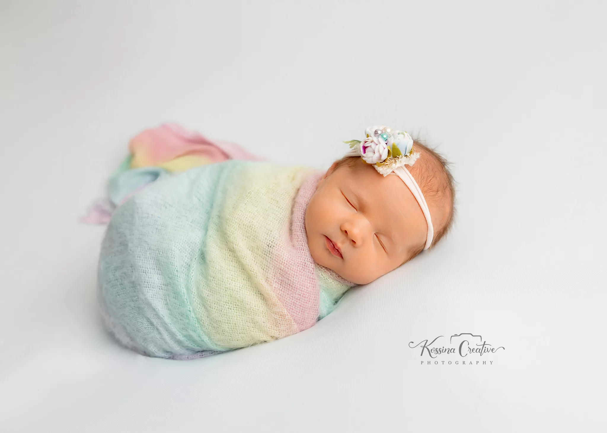 Orlando Newborn Photographer Baby Girl Photo studio pastel rainbow swaddle on white backgroud sleeping baby with rainbow flower headband